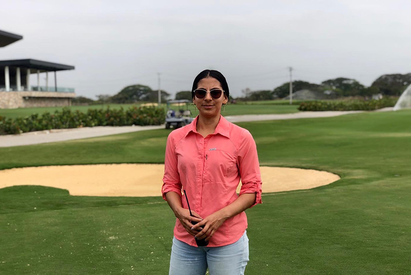 Woman in a pink button-up shirt and dark glasses stands outside on a golf course